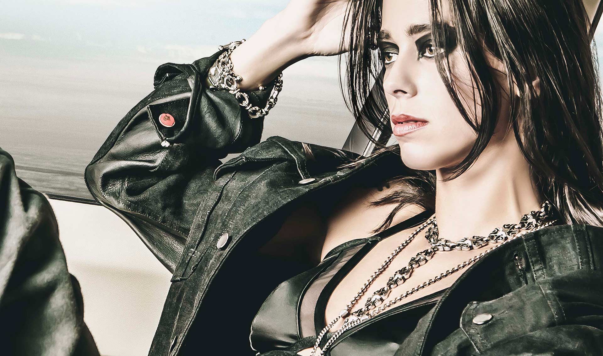 Woman sitting with legs up in a leather jacket and smokey eyes wearing jewelry