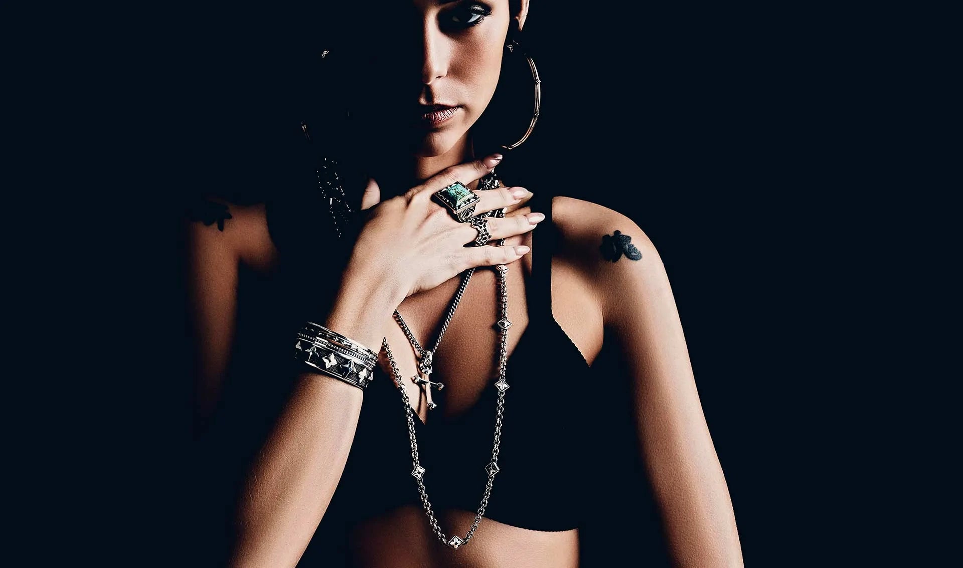 Woman standing on black backdrop with heavy shadows and striking jewelry